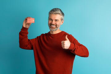 Cheerful mature man showing bank card and thumb up