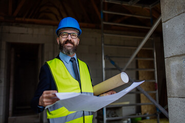 Mature businessman controlling blueprints from unfinished house.