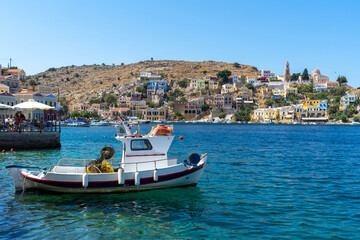 Fototapeta na wymiar Fishing or shrimp boat, shrimping boats or shrimpers with houses of Greek mountainous Symi Island, Dodecanese island chain. Harbor town of Symi and adjacent upper town Ano Symi