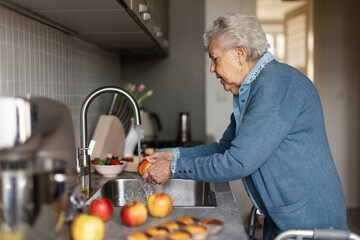 Happy senior woman washing apples in her kitchen.