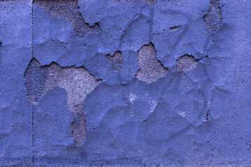 A surface of a concrete wall with huge chips in the blue plaster