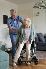 Obraz premium Caregiver helping senior woman to stand from her wheelchair in her home.