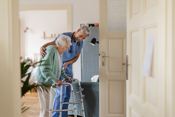 Caregiver helping senior woman to walk in her home with walker.