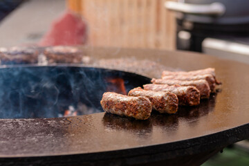 Process of grilling fresh pork sausages on brazier at summer local food market - close up. Outdoor cooking, barbecue, gastronomy, cookery and street food concept