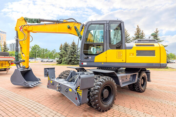 A large wheeled excavator is on display in a city square on a bright sunny spring day. Copy space.