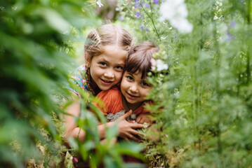 Cute children having fun outdoors. Two girls are playing hide and seek in the summer garden. Children among green nature. Little explorers.