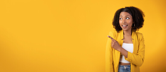 Excited happy black lady posing on yellow background and pointing aside at copy space, showing nice offer
