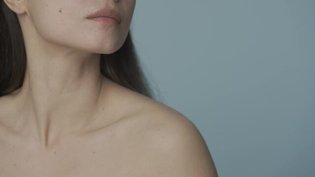 The seminude woman runs her well groomed hand over her chin and down to her neck. Close up of the perfect chin and slender neck of a woman on a blue background. SHDR BT2020 HLG Material.
