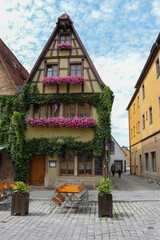 Fototapeta na wymiar Old historic Bavarian tavern house with beautiful pink flower window boxes. A woman and child walking along the narrow street, in Rothenberg Germany