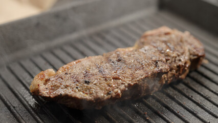 frying new york steak with tongs on grill pan