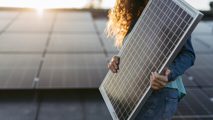 Close up of woman holding solar panel on the roof with photovoltaics panels.