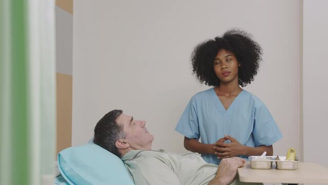 Friendly nurse talking to bedridden patient in hospital