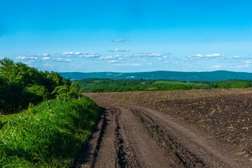 Fototapeta premium rural country road near a plowed field in the foothills of the Caucasus on a sunny summer day