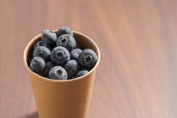 Fresh organic blueberries in papaer cup on wood table with copy space
