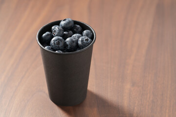 Blueberries in black paper cup on walnut table