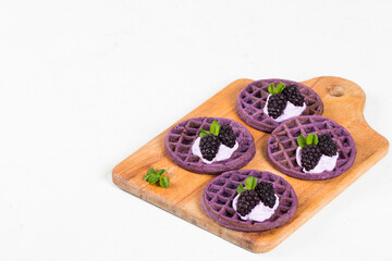 Vegan Purple round soft waffles with cream and blackberries on a wooden board. Waffles with the addition of natural blackberry puree. White background. Copy space
