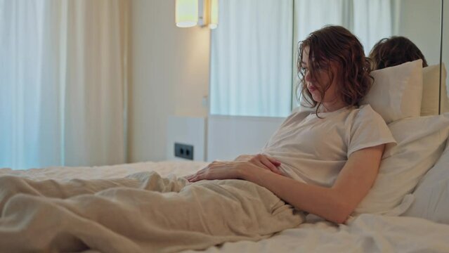 A young woman strokes a sick stomach while lying on the bed.