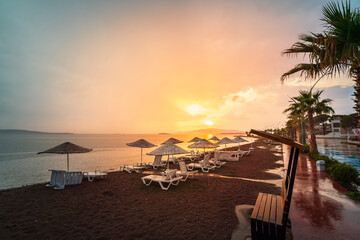 sunbeds tables and sunshade umbrellas located by the sea, trees and beach sand with a colorful...