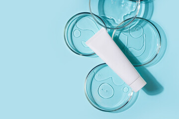 Cosmetic beauty concept with bottle serum, drops and petri dish on blue background