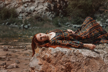 Strong-willed free strong red-haired woman in an ethnic dress near a big stone. A symbol of indomitability. Career