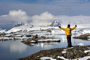 Photo of a man standing triumphantly atop a snow-covered mountain in Antarctica during a thrilling cruise tour