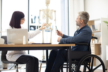 Full length view of female physician and man with disability examining skeleton model while staying...