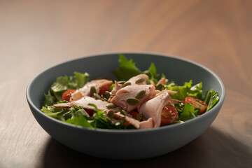 Salad with roasted turkey and cherry tomatoes decorated with pumpkin seeds in blue bowl