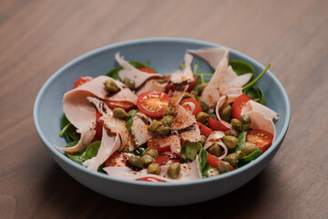 Salad with prosciutto cotto, cherry tomatoes and spinach in blue bowl