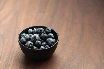 Big organic blueberries in a black bowl on walnut table