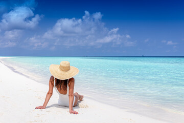 Fototapeta na wymiar A luxury tourist woman with sunhat sits on a tropical beach and enjoys the sun and turquoise sea
