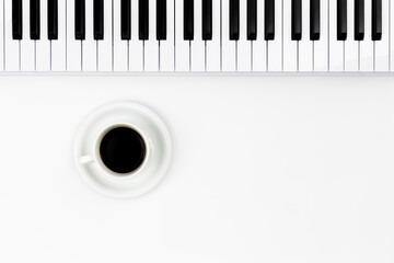 Naklejka premium Musical keyboard and a cup of coffee on a white background, flat lay, space for text. Minimalistic music background, conceptual minimalism.