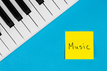 Piano keys and yellow paper reminder with handwritten lettering Music on a blue background, top view. The concept of musical creativity.