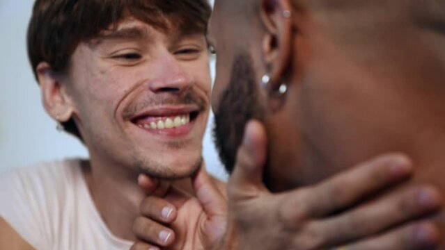 jovem casal gay inter racial brasileiro sentado na cama se olhando apaixonados