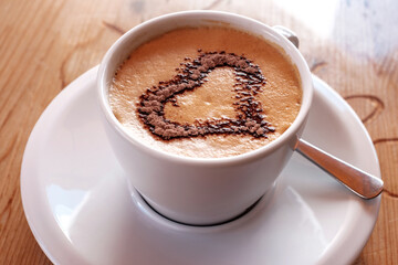 Cappuccino coffee in white cup with beautiful heart shape latte art on wooden table.