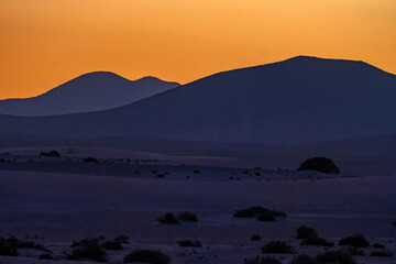 View of the dunes of Corralejo and silhouetted hills at sunset on the Canary Island of Fuerteventura, Spain.