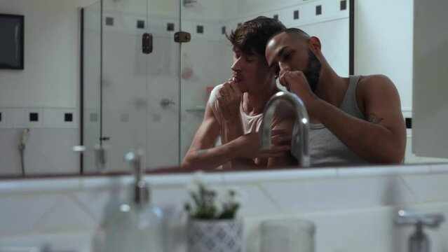 jovem casal gay inter racial brasileiro no banheiro escovando os dentes juntos sentados na banheira em frente ao espelho no dia dos namorados