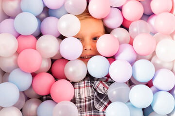 Little boy in a pool filled with plastic balls. Child peeking from pastel multi colored plastic balls for kids. top view.
