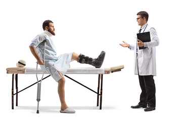 Injured man with an orthopedic boot and neck collar sitting on a therapy table and having conversation with a doctor