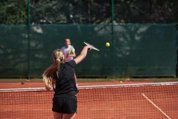 Young girls in a lively tennis match on a sunny day, demonstrating their skills and enthusiasm on a modern tennis court.