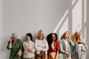 Multi-ethnic group of relaxed mature women bonding and smiling while leaning on the wall