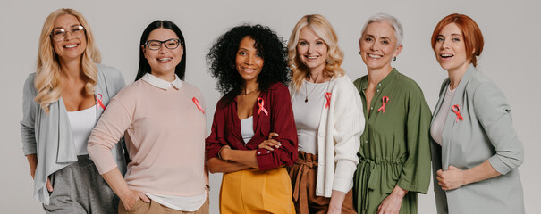Group of mature women wearing breast cancer ribbons and smiling against grey background