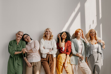 Multi-ethnic group of relaxed mature women bonding and smiling while leaning on the wall