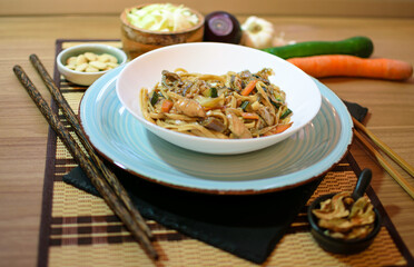 Rice noodles served with vegetables and meat in white bowl.