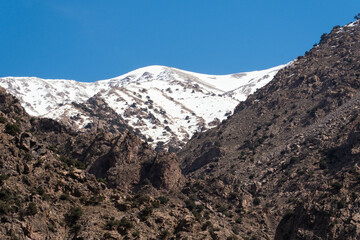 Peak of a snow mountain above the dirt mountains of the Ourika Valley in Morocco