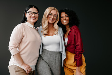 Three happy mature women bonding and smiling against grey background