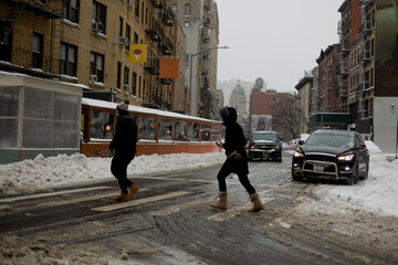 Two people cross a snowy city street
