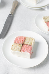 Battenburg cake on a white tray, almond and strawberry sponge cake covered in white fondant, pink and yellow check cake