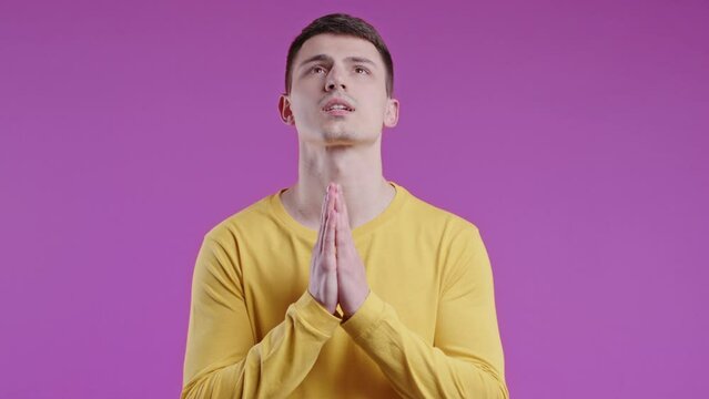 Young man praying with palms on pink background.Guy begs someone satisfy desires