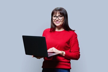 Fototapeta premium Friendly mature woman using laptop, over grey background