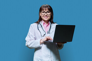 Mature female doctor using laptop on blue background